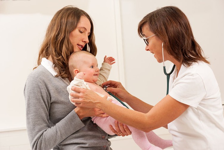 Eine Ärztin untersucht ein Baby auf dem Arm seiner Mutter