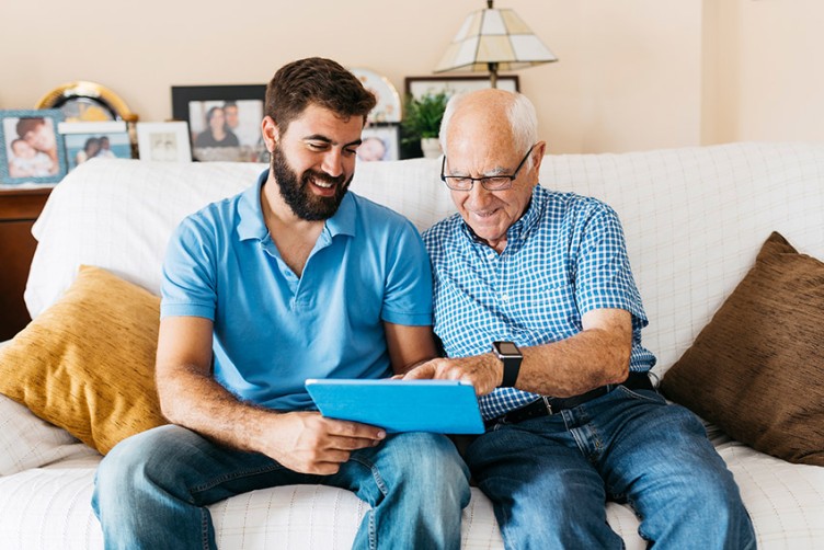 Ein älterer und ein jüngerer Mann im Pflegeheim arbeiten gemeinsam am Touchpad