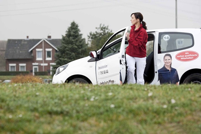 Eine Pflegekraft eines ambulantes Pflegedienstes steigt vor einem Einfamilienhaus aus dem Auto. 