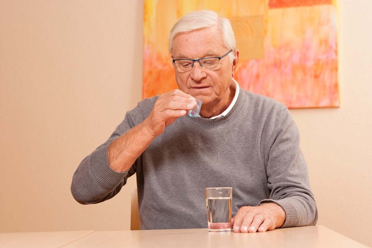 Ein älterer Mann nimmt Tabletten zu sich.
