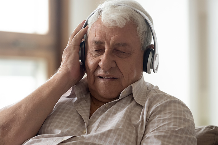 Ein älterer Mann mit Kopfhörern auf den Ohren hört etwas an.