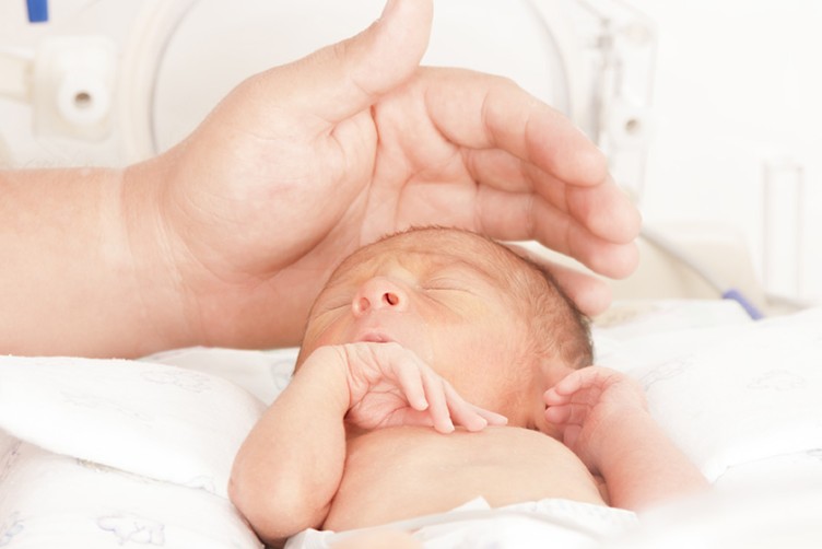 Ein Hand, die schützend über dem Kopf eines Neugeborenen liegt