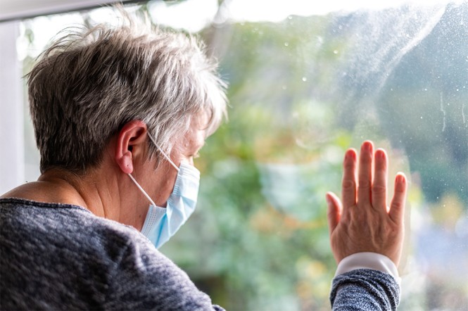 Eine ältere Frau mit Mundschutz schaut aus dem Fenster