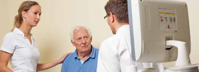 Zwei Pflegekräfte sprechen mit einem älteren Patienten