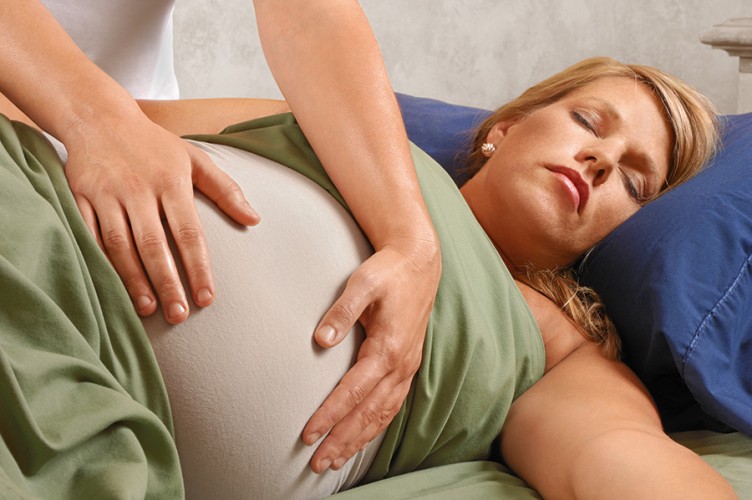 Eine Schwangere liegt auf dem Rücken, ihr Bauch wird massiert