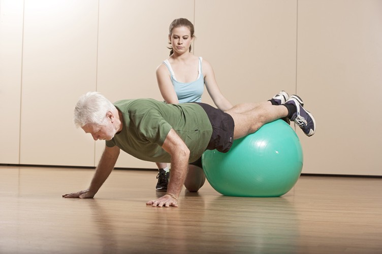 Eine Physiotherapeutin trainiert mit einem älteren Mann und einem Ball