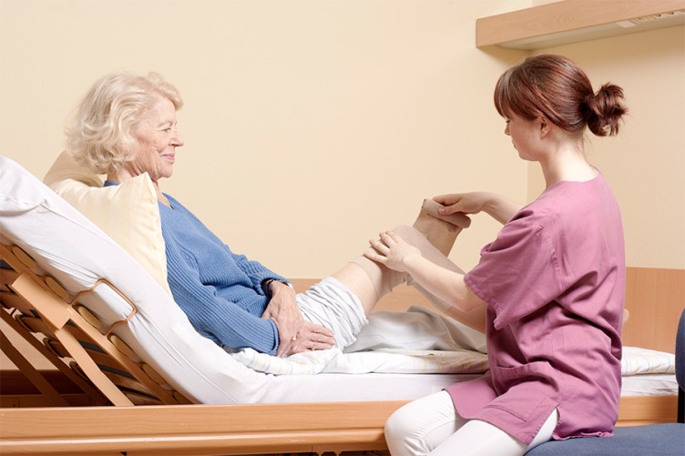 Eine Pflegerin verbindet das Bein einer älteren Patientin im Krankenbett