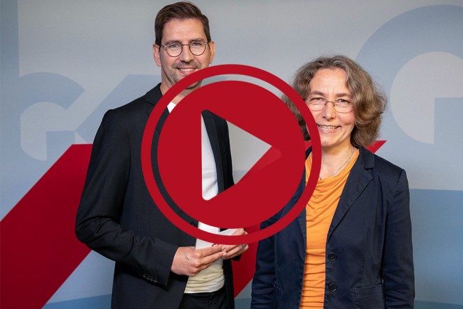 Fabian Fischer und Dr. Mechtild Schmedders vor einer Pressewand. Darüber ist ein großer roter Button mit einem Play-Symbol