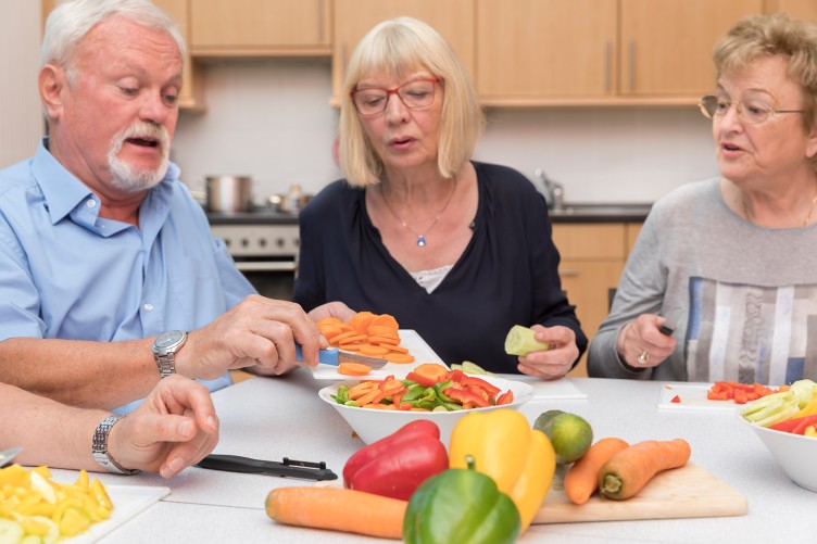 Drei Menschen an einem Tisch mit viel Gemüse besuchen einen Kochkurs