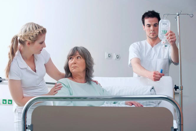Zwei Pflegekräfte kümmern sich um eine Patientin, die in einem Krankenhausbett liegt.
