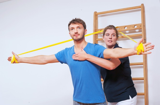 Eine Therapeutin hilft einem jungen Mann bei einer Übung mit Dehnbändern.