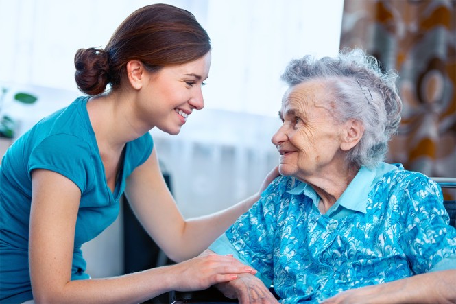 Eine Pflegekraft spricht mit einer älteren Dame in ihrem Wohnzimmer