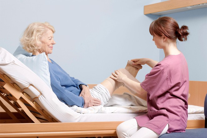 Eine Pflegekraft versorgt eine ältere Frau in einem Pflegebett